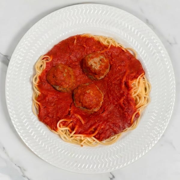 Spaghetti with three large meatballs and rich red marinara sauce on a white decorative plate.